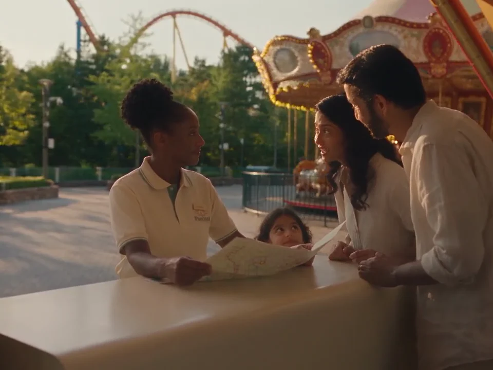 A guest-services host helps visitors with a map at a theme park.